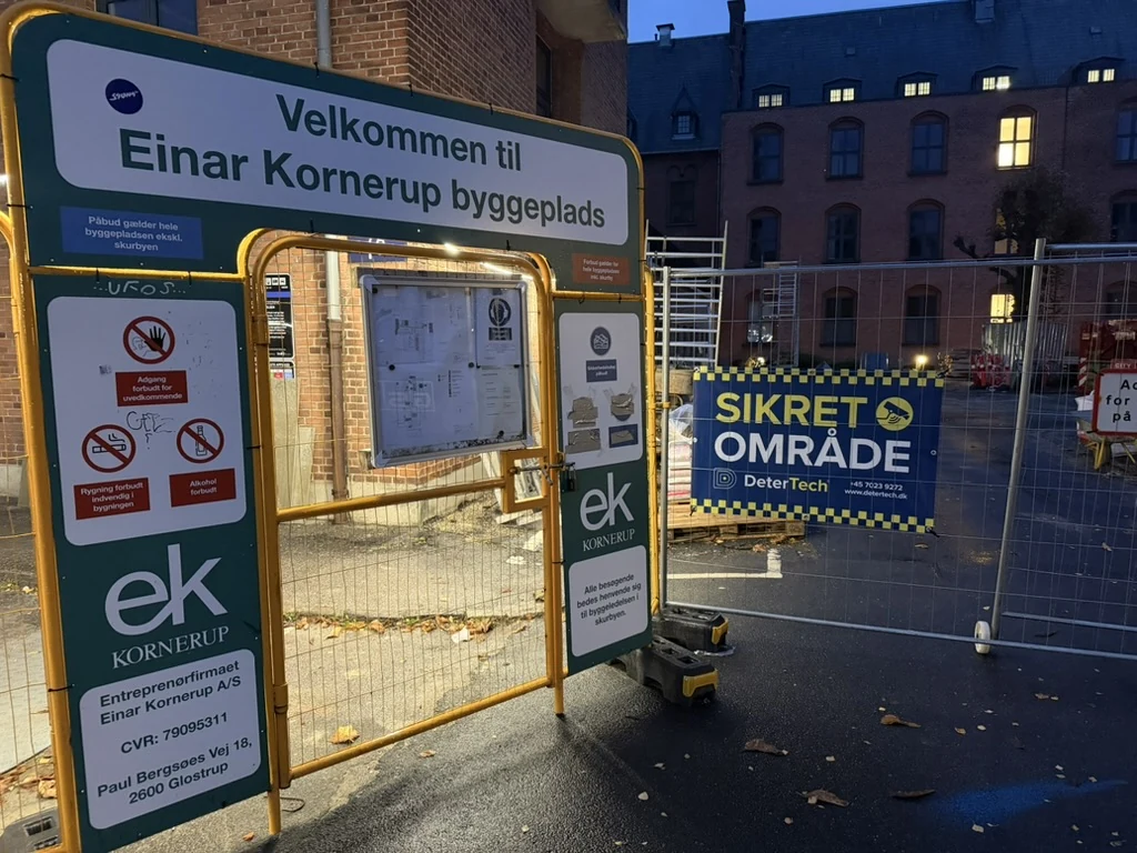 DeterTech-banner med SIKRET OMRÅDE på hegn ved byggepladsens gule adgangsport