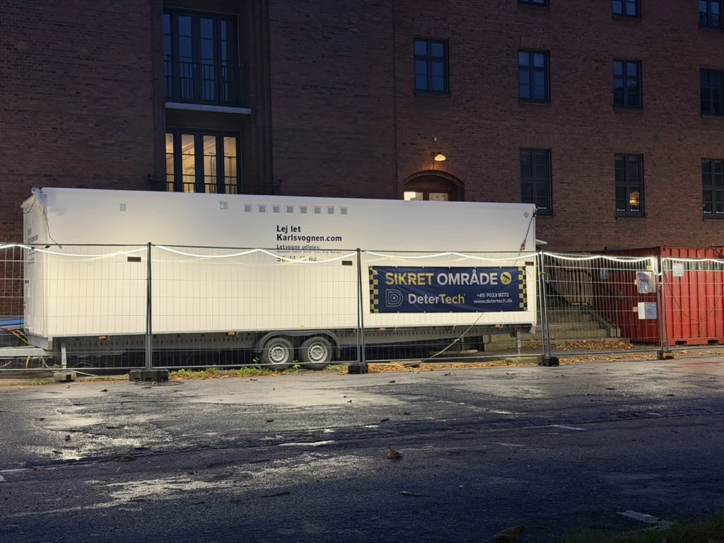 Bredt DeterTech-banner med SIKRET OMRÅDE på byggepladshegn foran en hvid skurvogn