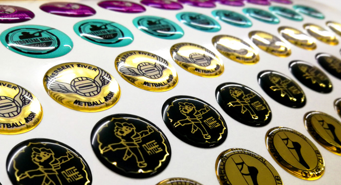Domed labels i guld, sort og turkis med logo
