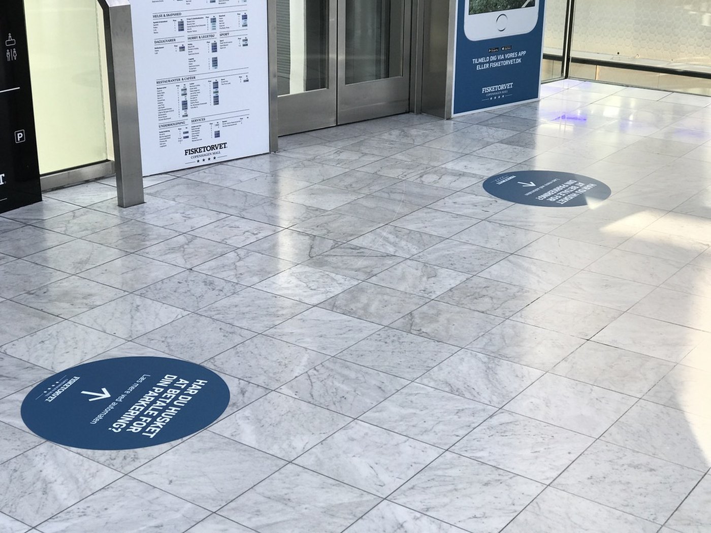 Gulvfolie med pil og wayfinding-budskab ved indgangsparti i indkøbscenter