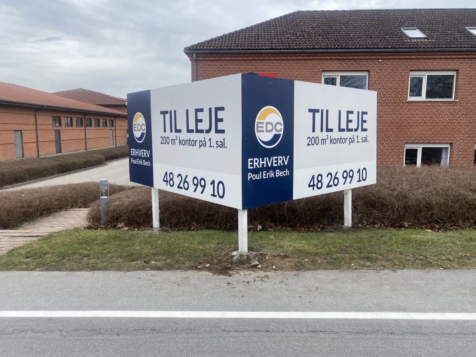 Specialbygget dobbeltsidet erhvervsskilt på stolper foran ejendom